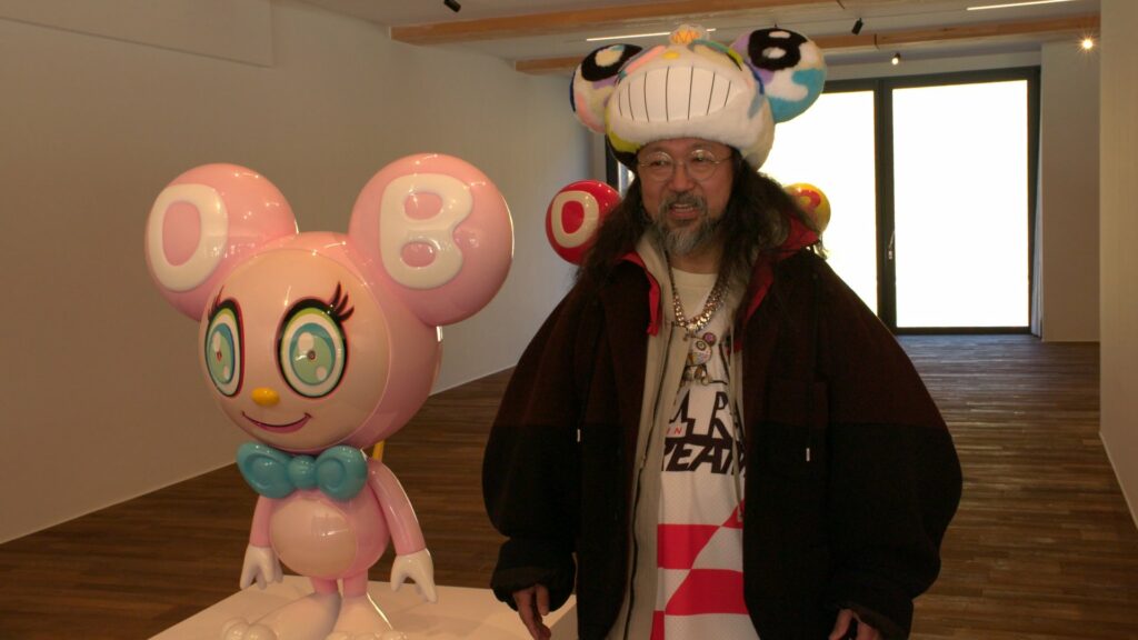 村上隆與其最具代表性的角色Mr. DOB，這個自1993年誕生的形象，從可愛到怪誕不斷變形，成為其「超扁平」藝術中最具辨識度的角色。